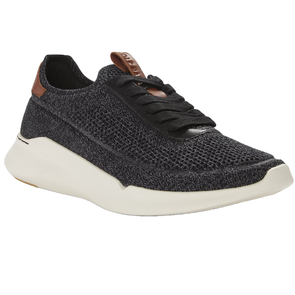 The Cole Haan Grand Crosscourt Sneakers feature a dark textured knit upper with black laces and brown accents on the heel tab. They have a sleek white sole that provides a modern, sporty look.