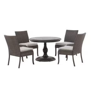 A round outdoor dining set with a central pedestal table and four wicker chairs featuring light cushions.