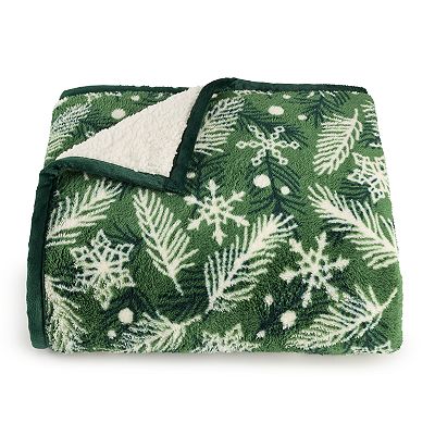 Green sherpa throw blanket with a white snowflake and pine needle design, featuring a white underside for contrast.