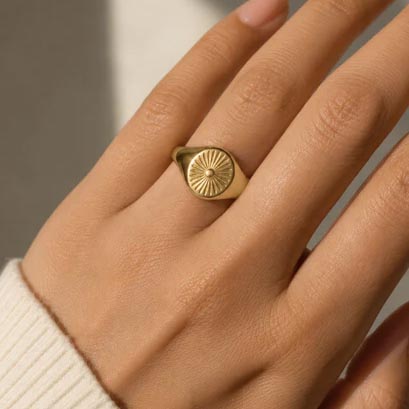 A hand wearing a gold signet ring with a sunburst design.