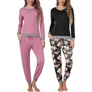 Two women are wearing comfortable pajama sets; one is pink with grey accents, and the other is a black top with floral-print pants, both featuring long sleeves and cuffed hems.