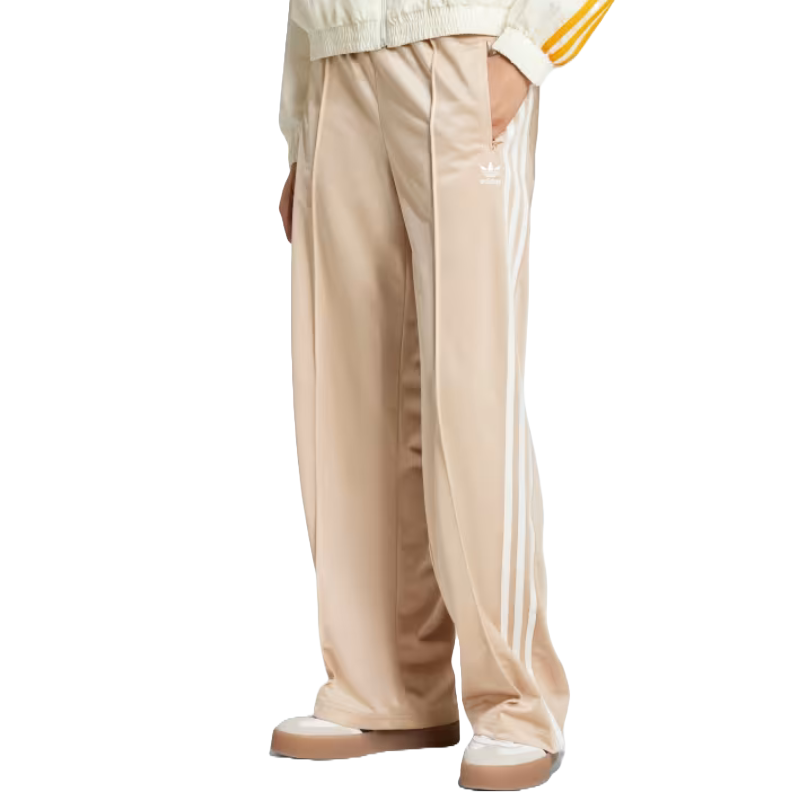 Beige Adidas track pants with three side stripes and a small logo, paired with two-toned sneakers.