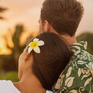 Two people embracing, one with a green and white patterned shirt and the other with a white flower in their hair.
