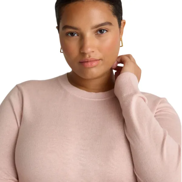 A person wearing a light pink long-sleeve knit top with a crew neckline and gold hoop earrings.