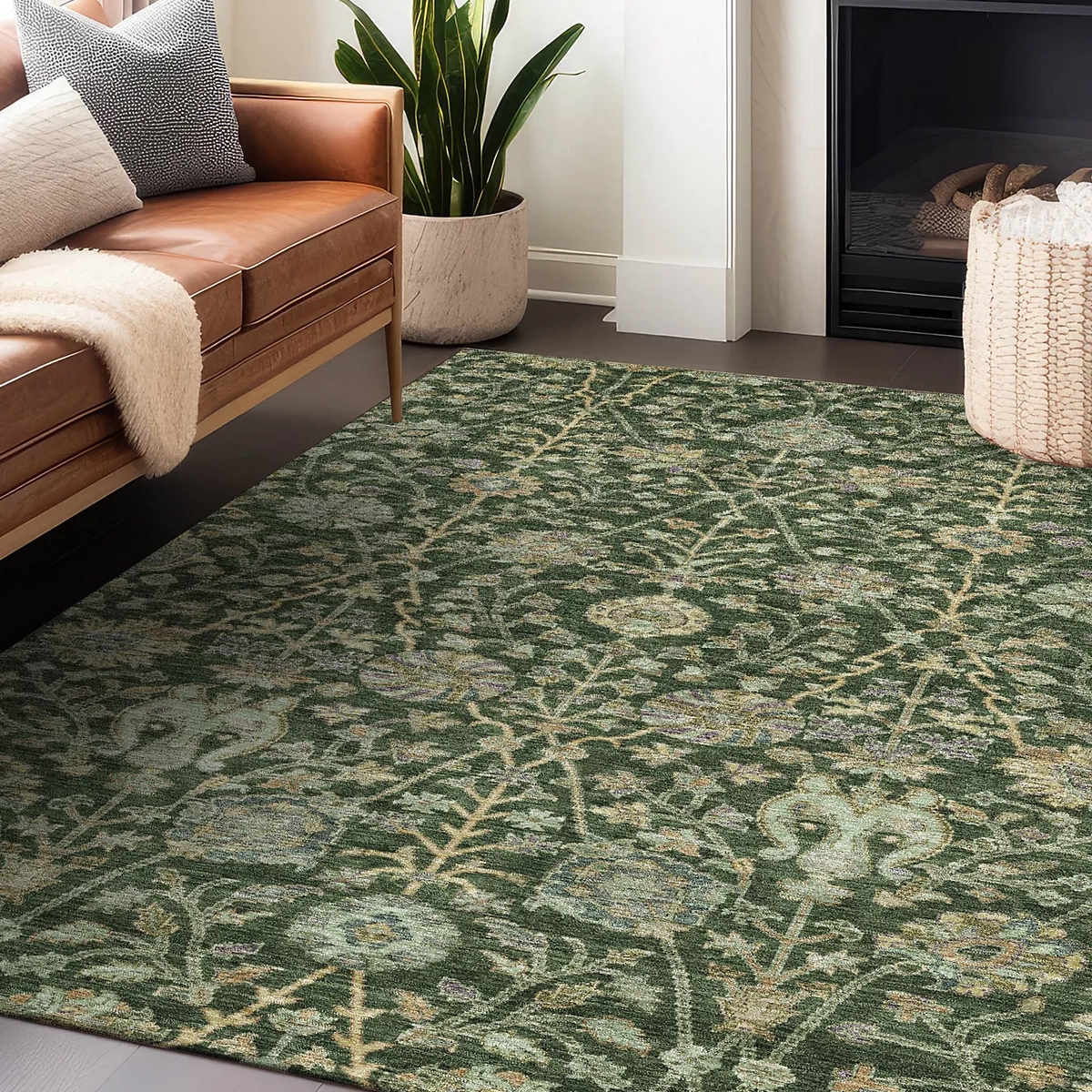 A green, washable rug featuring a floral pattern with intricate vine designs, situated in a living room beside a leather sofa, a large plant, and a fireplace.