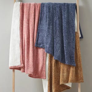 A variety of bath towels in different colors, including white, pink, blue, and brown, are hanging on a wooden rack.