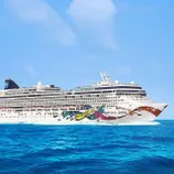 A large white cruise ship with colorful artwork on the bow, named \“Norwegian Jewel,\“ sails on blue ocean waters under a clear sky.