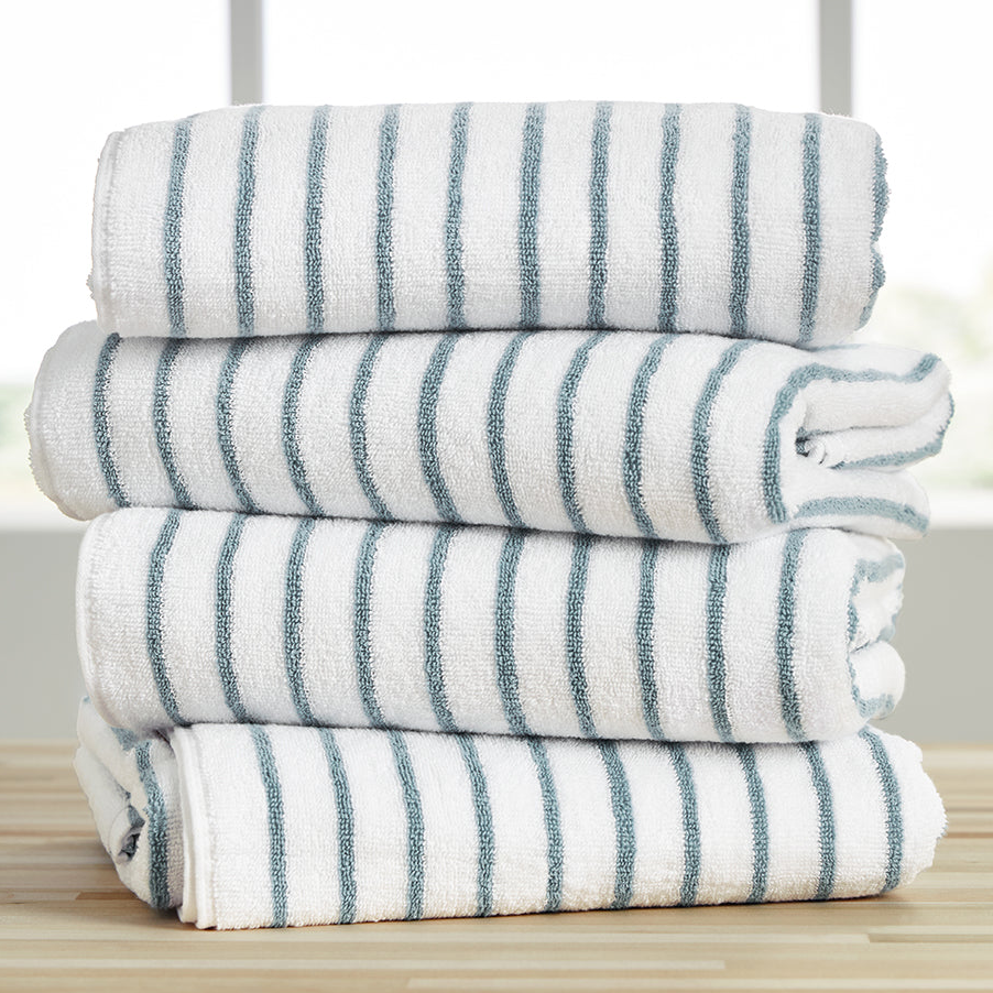A stack of four oversized cotton cabana towels with white and blue stripes, neatly folded on a wooden surface.