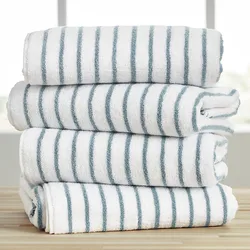 A stack of four oversized cotton cabana towels with white and blue stripes, neatly folded on a wooden surface.