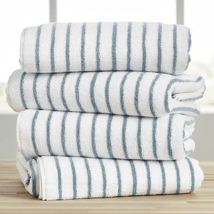 A stack of four oversized cotton cabana towels with white and blue stripes, neatly folded on a wooden surface.