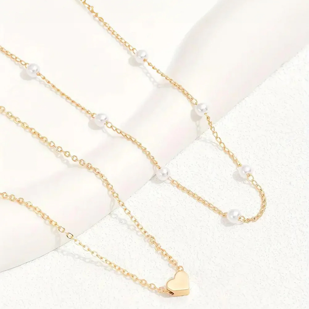 A two-piece necklace set featuring gold chains; one adorned with small pearls and the other with a heart pendant.