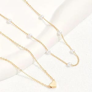 A two-piece necklace set featuring gold chains; one adorned with small pearls and the other with a heart pendant.