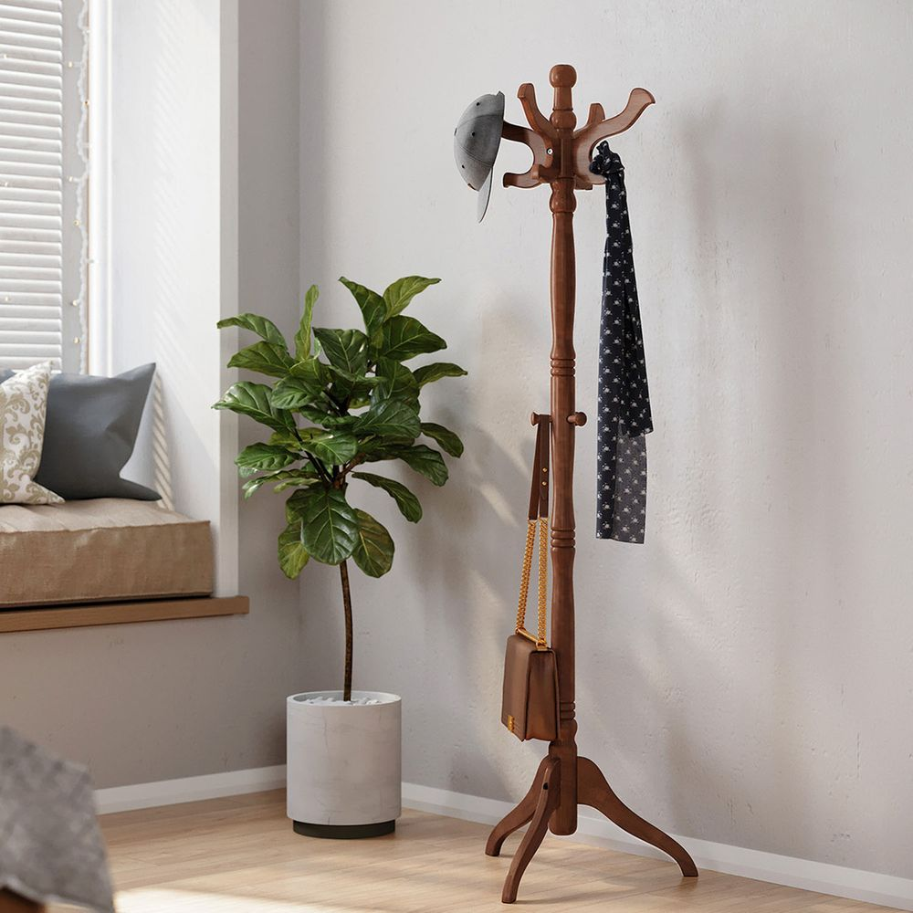 A wooden coat rack stands with a cap, scarf, and bag hanging on it, next to a green potted plant.