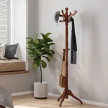 A wooden coat rack stands with a cap, scarf, and bag hanging on it, next to a green potted plant.
