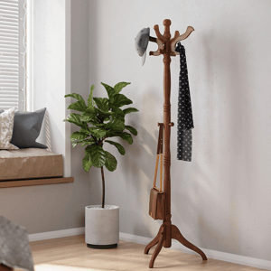 A wooden coat rack stands with a cap, scarf, and bag hanging on it, next to a green potted plant.