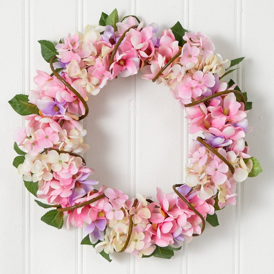 A floral wreath composed of pink and white hydrangea blooms with green leaves.
