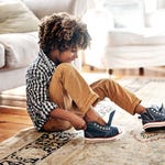 A child tying the laces of blue sneakers with white soles.