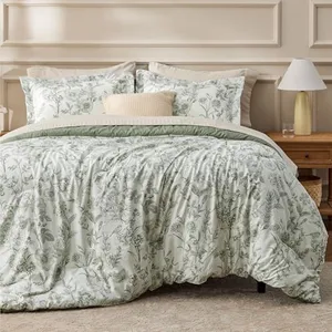A bed set featuring a floral-patterned comforter and pillow shams in soft green tones, complemented by a neutral decorative pillow. A wooden nightstand is visible beside the bed with a lamp and small objects placed on it.