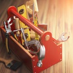 A red toolbox with various hand tools including a hammer, wrench, pliers, screwdrivers, and a paintbrush on a wooden surface.
