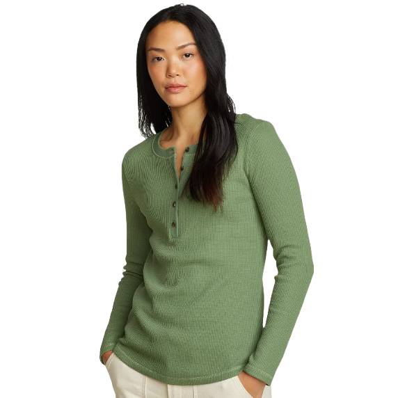 A person is wearing a long-sleeve, green thermal Henley shirt with a waffle knit texture and a buttoned neckline, paired with light-colored pants, hands in pockets.