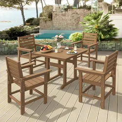 A patio set featuring a rectangular wooden table and four matching chairs with armrests, placed on a deck by a pool, surrounded by lush greenery and a stone wall.