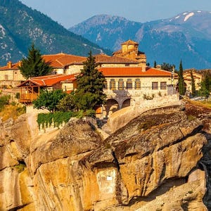 A historic monastery built on top of a rugged rock formation, surrounded by mountainous scenery.