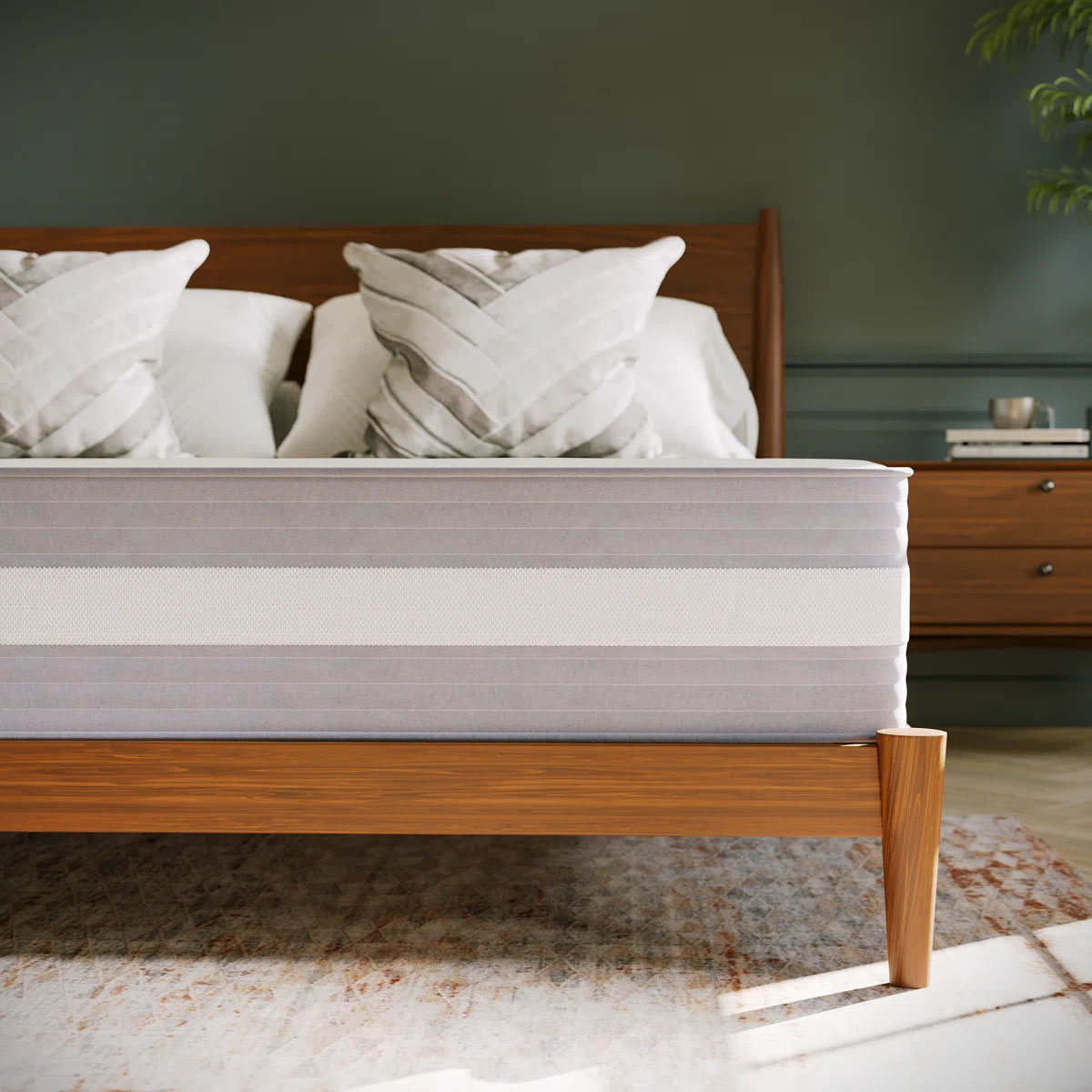 A wooden bed frame with a striped mattress is shown, accompanied by three decorative pillows in a bedroom setting with a nightstand and a plant in the background.