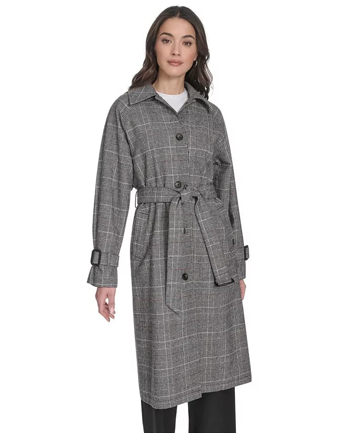 A woman is wearing a gray plaid trench coat with a tie belt and buttoned details.