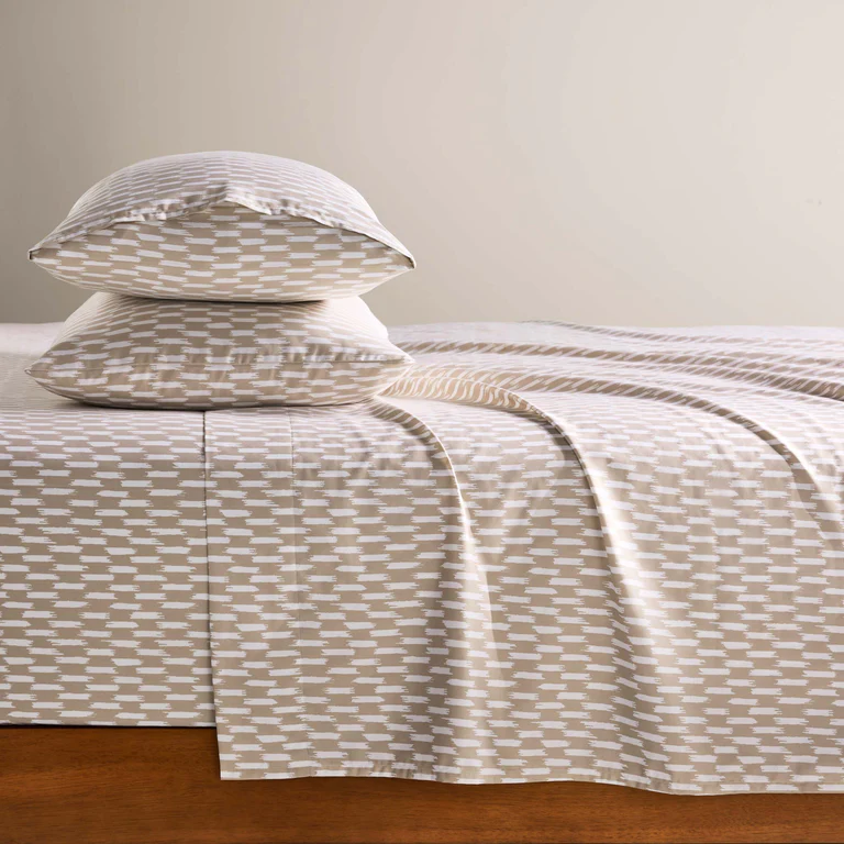 A set of bed sheets and pillowcases featuring a beige and white geometric pattern, neatly arranged on a wooden bed frame.