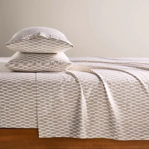A set of bed sheets and pillowcases featuring a beige and white geometric pattern, neatly arranged on a wooden bed frame.