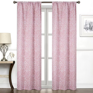 Pink curtains with a white paisley pattern hang on a rod in front of a window. The room features a table with a lamp and a small potted plant, along with framed wall art.