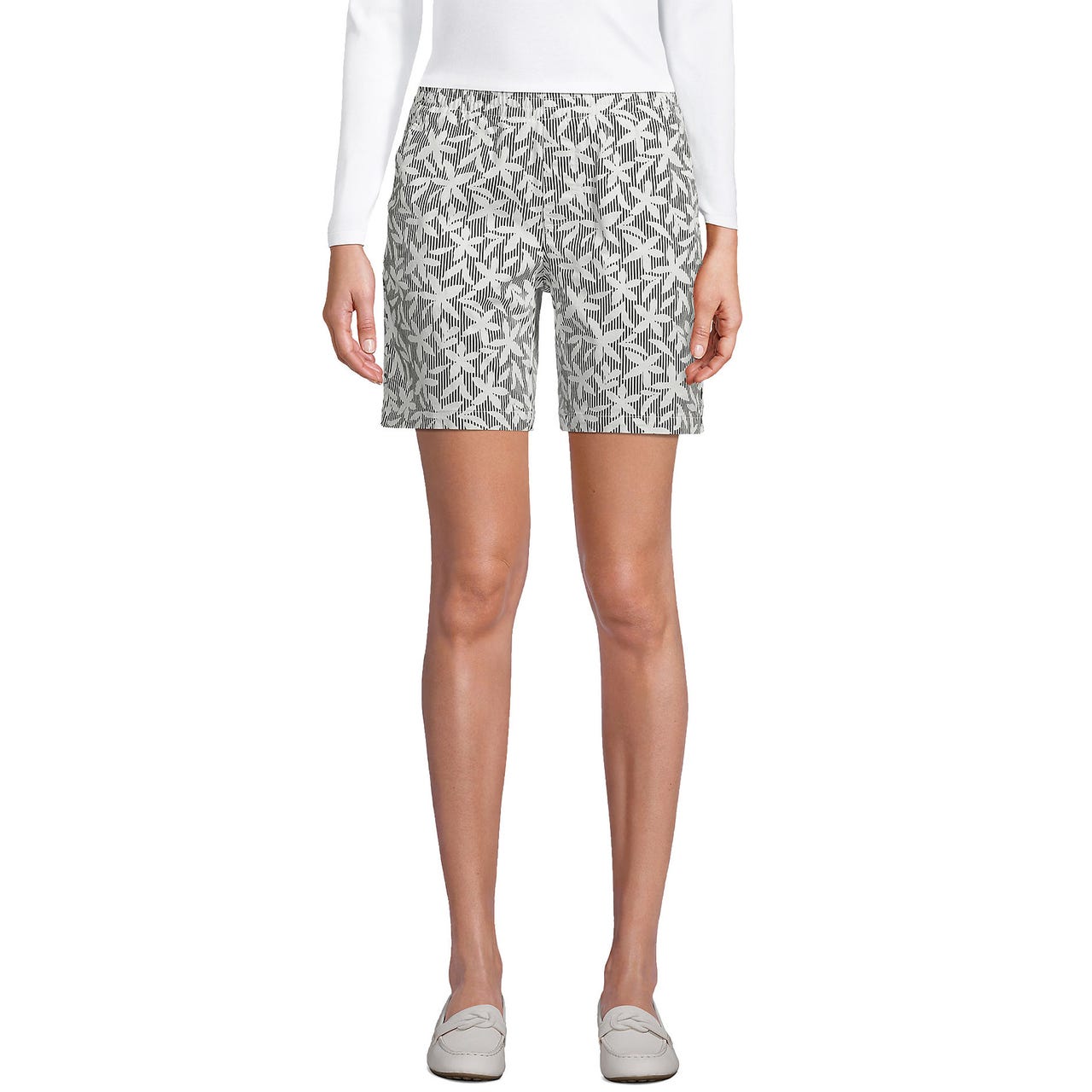 A pair of patterned shorts with a white long-sleeve top and white loafers.