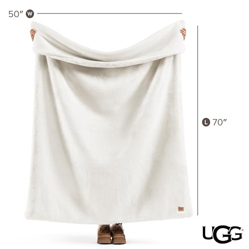 UGG blanket measuring 50\“ W x 70\“ L, shown in white being held by two hands and a pair of boots visible at the bottom.