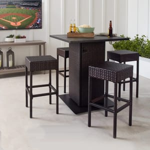 A dark brown wicker bar set with four stools and one rectangular bar table, set in an indoor space with decorative plants and a televised sports game in the background.