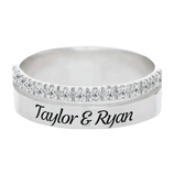 A silver ring featuring a row of small diamonds on the top half and engraved with the names \“Taylor & Ryan\“ on the band.