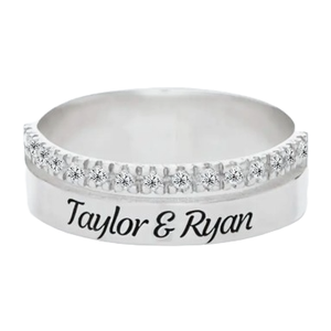 A silver ring featuring a row of small diamonds on the top half and engraved with the names \“Taylor & Ryan\“ on the band.
