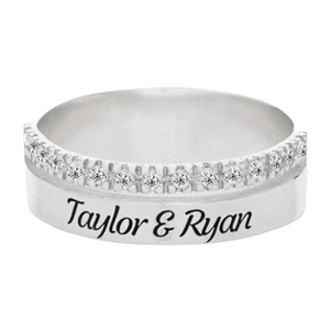 A silver ring featuring a row of small diamonds on the top half and engraved with the names \“Taylor & Ryan\“ on the band.