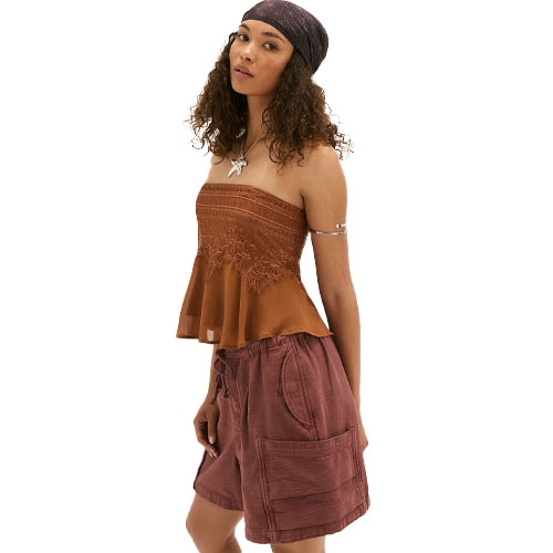 A woman wearing a brown strapless top with lace detailing, mauve shorts with pockets, and a headscarf, accessorized with a star necklace and arm cuff.
