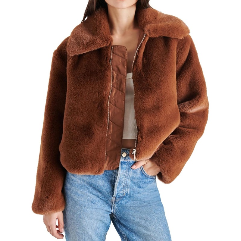 A brown faux fur coat with a wide collar and a zipper closure, worn over a white top and blue jeans. The fabric appears soft and plush, providing a cozy look.