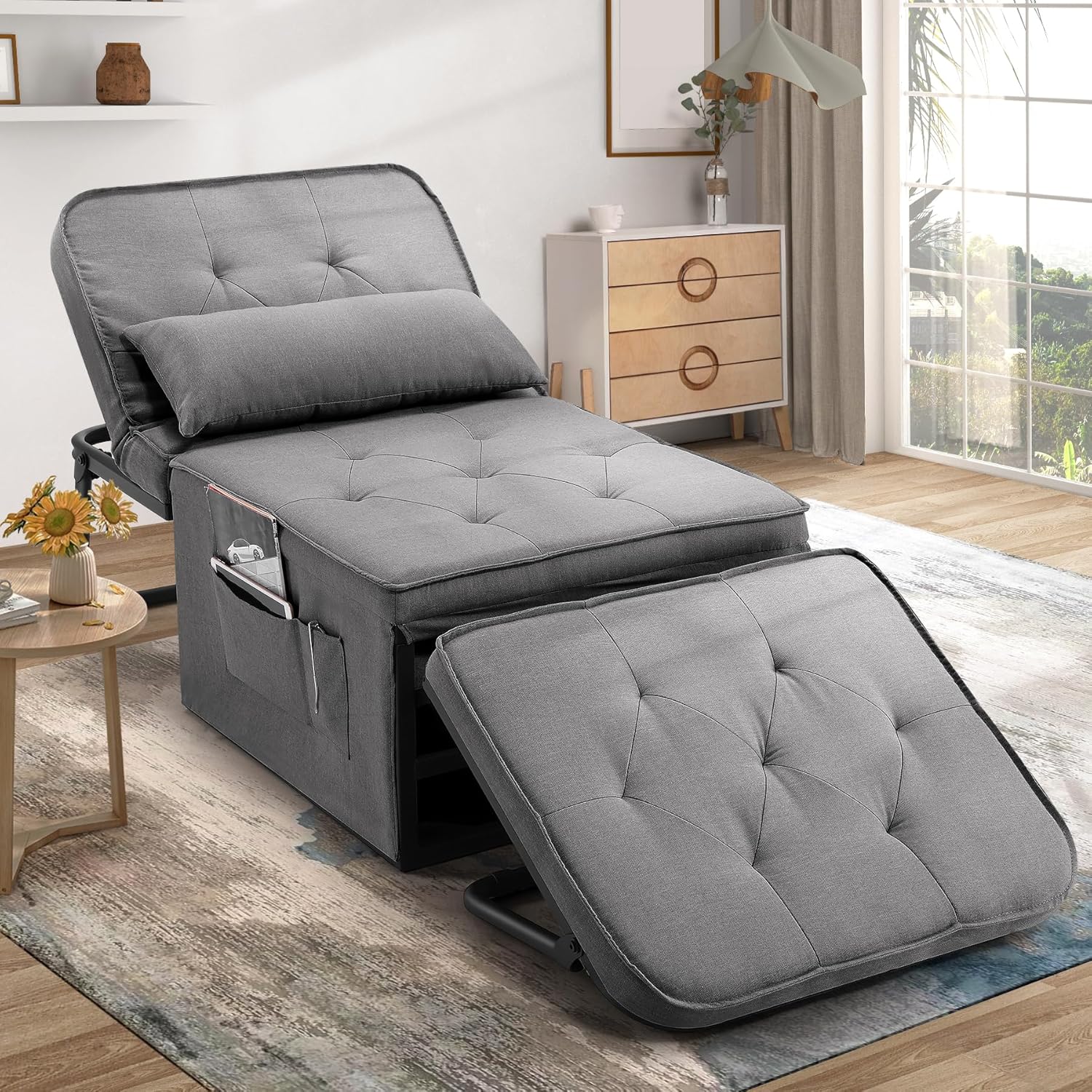 An adjustable gray chair bed with tufted cushioning is extended outwards, featuring a storage pocket and a detachable footrest.