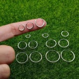 A variety of silver hoop earrings are displayed on a person's finger and arranged on green grass, showcasing different sizes.