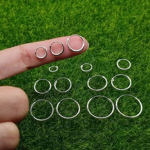 A variety of silver hoop earrings are displayed on a person's finger and arranged on green grass, showcasing different sizes.