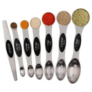 A set of stainless steel measuring spoons with capacities ranging from 1/8 teaspoon to 1 tablespoon, each filled with different spices, includes a leveling tool.