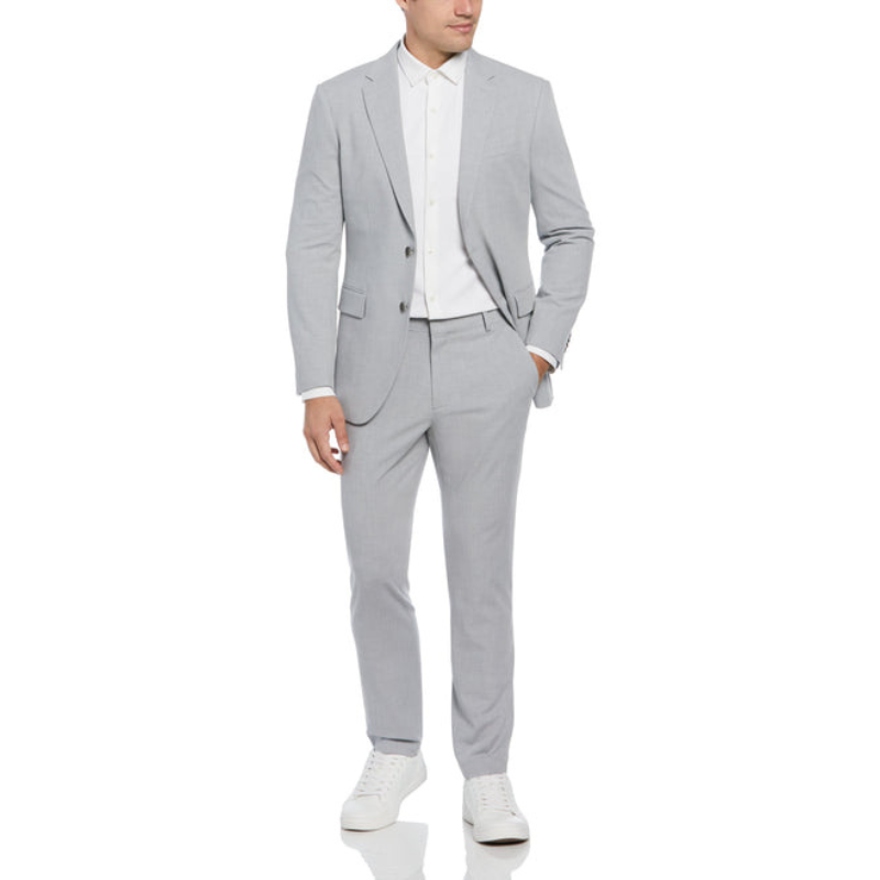 A man wears a slim-fit, light-grey Louis suit with a white dress shirt and matching trousers, paired with white sneakers. The suit features a two-button jacket and a modern, tailored silhouette.