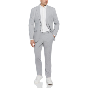 A man wears a slim-fit, light-grey Louis suit with a white dress shirt and matching trousers, paired with white sneakers. The suit features a two-button jacket and a modern, tailored silhouette.