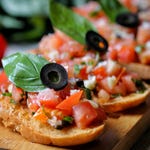 Bruschetta with diced tomatoes, black olives, and basil on toasted bread.