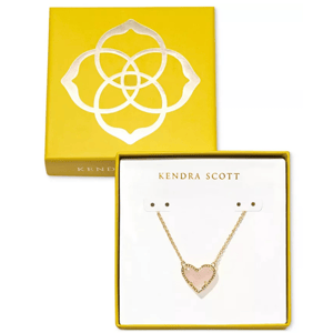 Kendra Scott Boxed Heart Necklace features a pink heart-shaped pendant on a gold chain, packaged in a yellow box with a floral design.