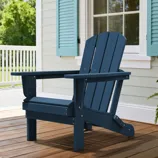 A navy blue Adirondack chair is placed on a wooden porch with light blue shutters and a white railing in the background.