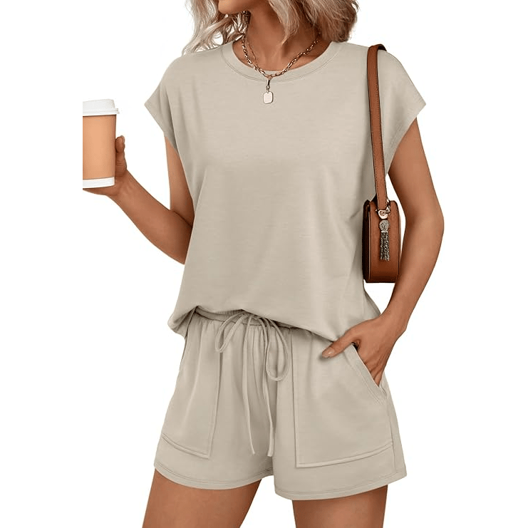 A woman wearing a casual beige short-sleeve top and matching drawstring shorts, accessorized with a brown shoulder bag and necklace, holding a coffee cup.