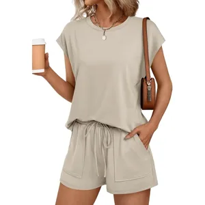 A woman wearing a casual beige short-sleeve top and matching drawstring shorts, accessorized with a brown shoulder bag and necklace, holding a coffee cup.